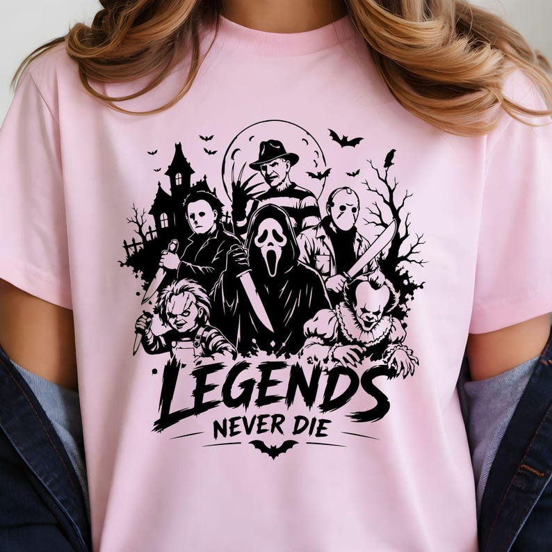 May include: A light pink t-shirt featuring a black graphic print of various horror movie characters, including a masked figure, a doll, and a clown, set against a haunted house and moon background with the text "LEGENDS NEVER DIE" below.