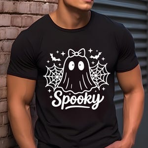 May include: Black t-shirt with a white graphic of a ghost wearing a bow, surrounded by spiderwebs, bats, and stars. The word "Spooky" is written in a script font below the ghost. Halloween-themed apparel.