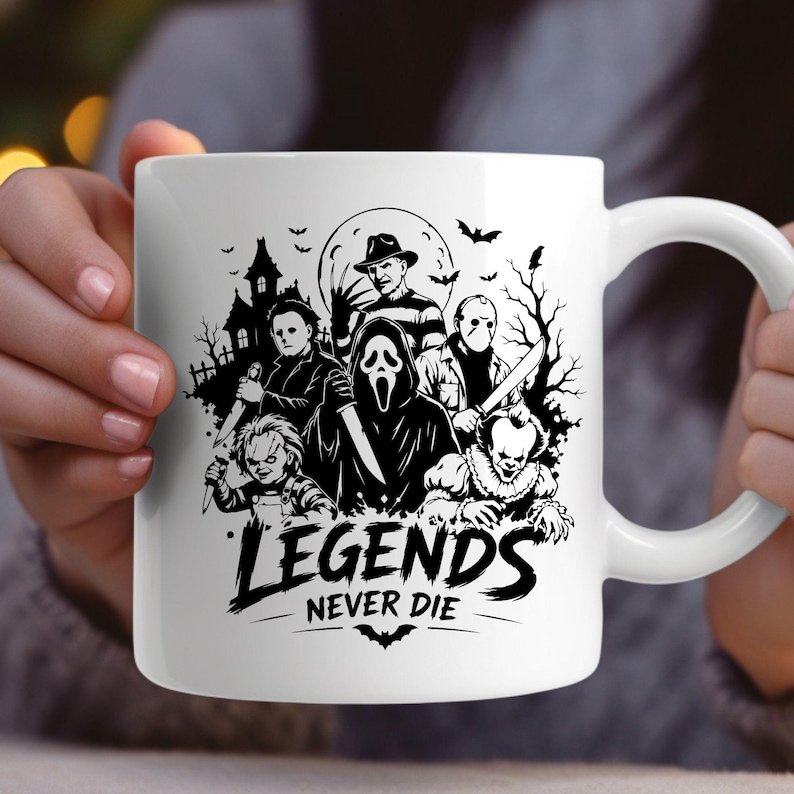 May include: A white ceramic mug featuring a black graphic print of various horror movie characters, including a masked figure, a clown, and a doll, set against a haunted house and moon background with the text "LEGENDS NEVER DIE" at the bottom.
