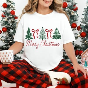 以下が含まれることがあります： クリスマスツリーのデザインと赤い「Merry Christmas」の文字が入った白いTシャツ。緑のクリスマスツリーと赤いリボンが特徴です。赤と黒のチェック柄のパジャマパンツと白い靴下を履いています。