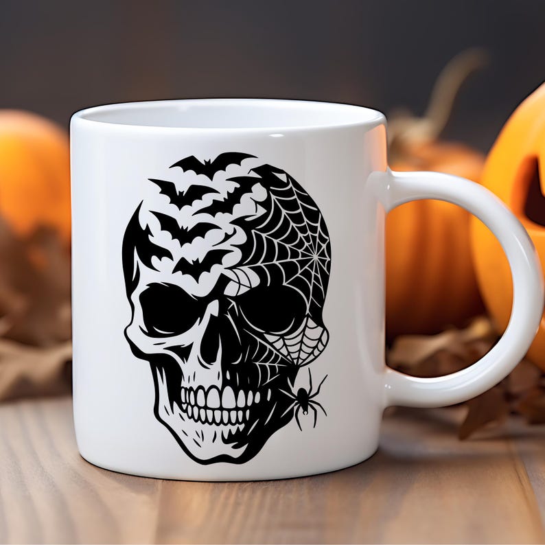May include: White ceramic mug with a black skull design, bats, a spider web, and a spider. The Halloween-themed mug has a curved handle. The background is blurred, showing pumpkins and autumn leaves.