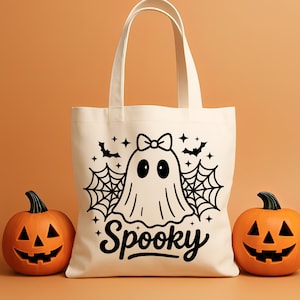 May include: A cream-colored tote bag with a black ghost design, bats, spiderwebs, and the word "Spooky." Two carved orange pumpkins flank the bag. The bag has two handles and is made of a sturdy fabric.