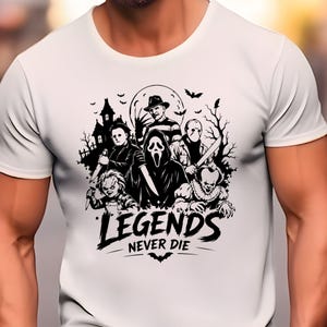 May include: A white short-sleeved t-shirt featuring a black graphic print of various horror movie characters, a haunted house, and bats. The text "LEGENDS NEVER DIE" is printed in a bold, stylized font at the bottom of the central illustration.