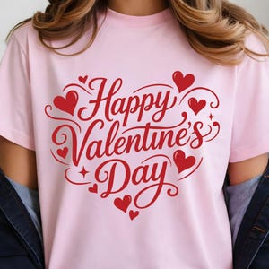 May include: A light pink t-shirt with the words "Happy Valentine's Day" in red script. The design includes red hearts and decorative swirls, perfect for celebrating the holiday of love.