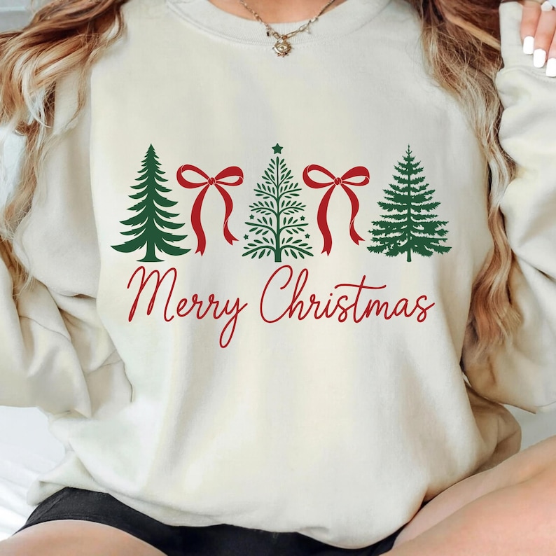 以下が含まれることがあります： クリーム色のスウェットシャツ。デザインは、4本の緑のクリスマスツリー、2つの赤いリボン、そして赤い筆記体で書かれた「Merry Christmas」の文字が特徴です。暖かく、季節感のあるアパレルアイテムです。