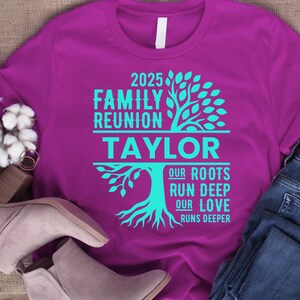 May include: A purple t-shirt with turquoise text and a tree graphic. The text reads "2025 Family Reunion Taylor" with the words "Our Roots Run Deep Our Love Runs Deeper" below the name. The shirt is paired with jeans and shoes.