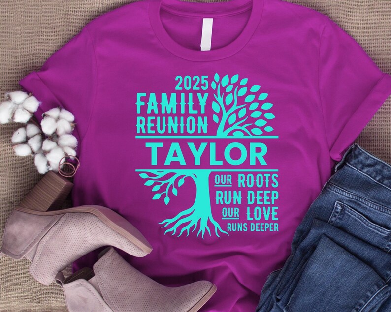 May include: A purple t-shirt with turquoise text and a tree graphic. The text reads "2025 Family Reunion Taylor" with the words "Our Roots Run Deep Our Love Runs Deeper" below the name. The shirt is paired with jeans and shoes.