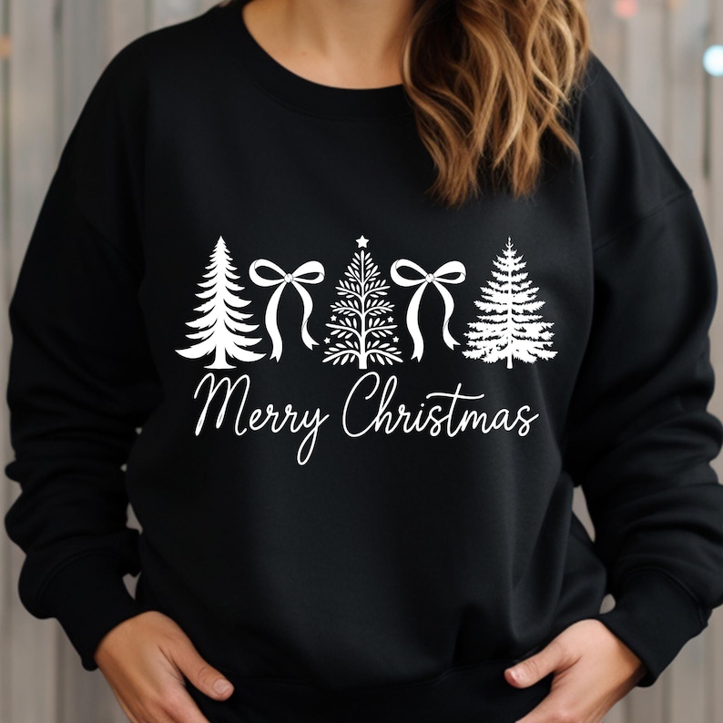 以下が含まれることがあります： 黒いスウェットシャツに、4本のクリスマスツリーとリボンの白いグラフィック。 「Merry Christmas」の文字が筆記体で下に書かれています。 シンプルでフェスティバルなデザイン。