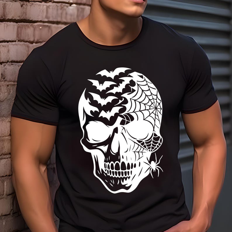 May include: Black t-shirt with a white skull design incorporating bats, a spider web, and a spider. The graphic is a Halloween-themed illustration. The shirt has a crew neck and short sleeves.