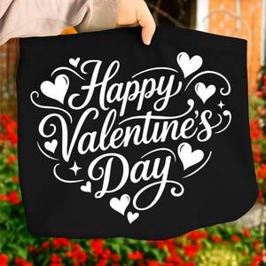 May include: Black tote bag with the words "Happy Valentine's Day" in white script, adorned with white hearts and decorative swirls. The bag is held up by a person.