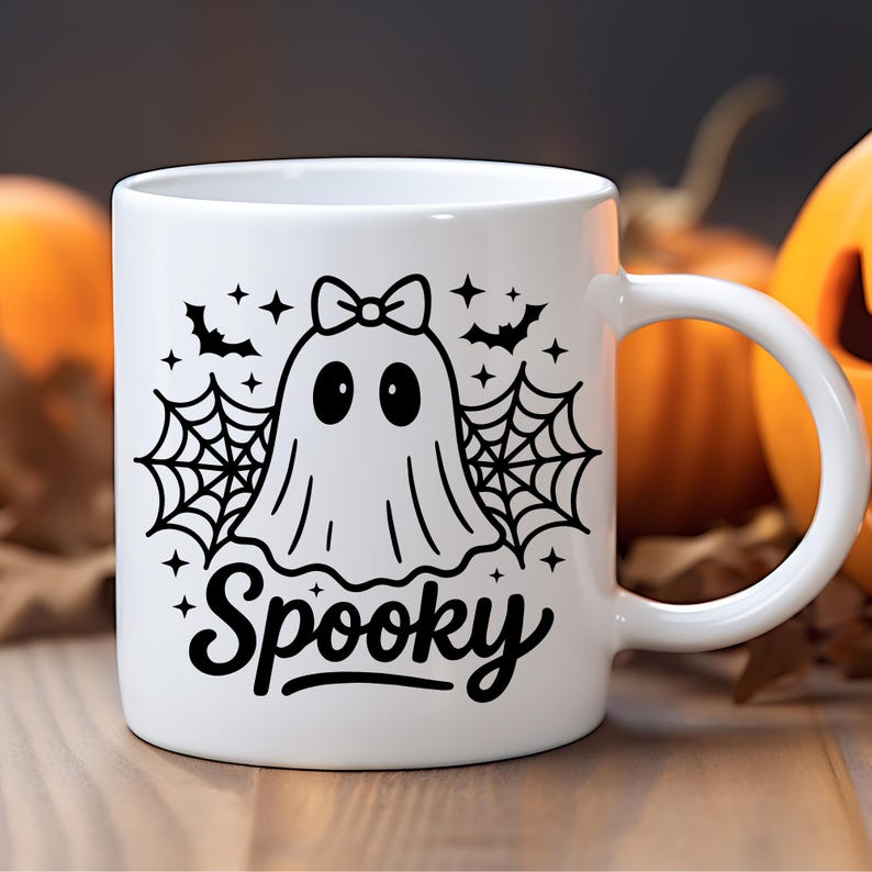 May include: White ceramic mug with a black graphic of a ghost wearing a bow, spiderwebs, bats, and stars. The word "Spooky" is written in a script font. Perfect for Halloween or spooky season.