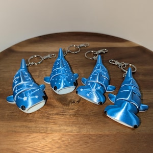 May include: Four articulated shark keychains in a metallic blue finish with white constellation patterns. Two keychains are whale sharks and two are hammerhead sharks, each featuring a silver-toned metal split ring and a lobster claw clasp.