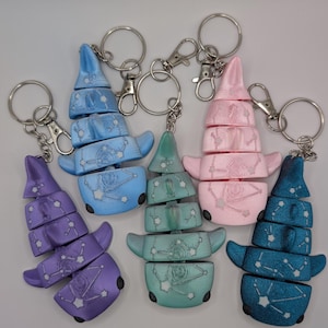 May include: Five articulated shark keychains in purple, light blue, teal, pink, and dark blue. Each shark features a 3D-printed texture with a white constellation pattern across the body, a segmented design, and a silver metal keyring attachment.