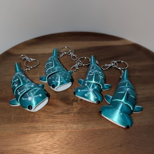May include: Four articulated shark keychains in a metallic teal finish. Two are whale sharks and two are hammerhead sharks, each featuring white constellation patterns on their backs, black eyes, and silver-toned metal lobster claw clasps.