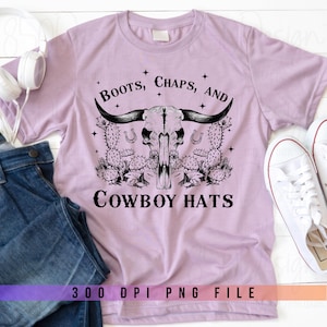 Könnte beinhalten: Ein helllila T-Shirt mit einem schwarzen Grafikdesign eines Schädels mit Hörnern, Kakteen und dem Text "Boots, Chaps, and Cowboy Hats".