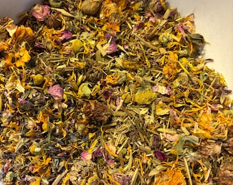 May include: A loose leaf herbal tea blend featuring dried chamomile flowers, vibrant orange calendula petals, pink rose petals, and various green botanical stems and leaves, all contained within a white bowl.