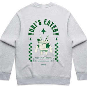 May include: A pale grey sweatshirt with a green graphic. The graphic says "Yuki's Eatery" and features a cartoon food container with chopsticks. The text "FOOD • FUN • RACING" is also present, along with the brand name "MOUVE."
