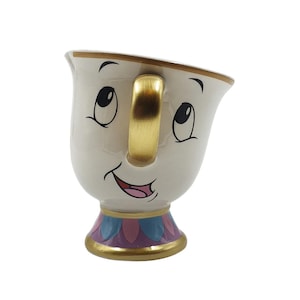May include: A white ceramic teacup with a smiling face, gold handle, and gold trim. The base of the cup has a decorative design with pink, blue, and purple accents. The teacup is a character from a popular animated film.
