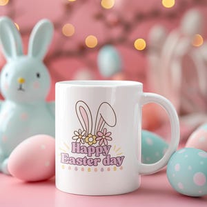 Puede incluir: Taza de cerámica blanca con un diseño de conejo rosa y el texto "Happy Easter Day". La taza está rodeada de huevos de Pascua de colores pastel.
