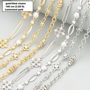 Puede incluir: Una colección de cadenas chapadas en oro y de tono plateado que miden 100 cm de largo. Las cadenas presentan eslabones alternos que incluyen dijes en forma de flor con piedras transparentes, perlas blancas, eslabones ovalados y cuentas texturizadas.