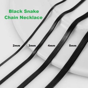 Peut inclure: Colliers chaîne serpent noirs de différentes largeurs : 2 mm, 3 mm, 4 mm et 5 mm. Le texte "Black Snake Chain Necklace" est en vert. Les colliers sont présentés sur une surface blanche.