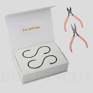 May include: A white box with the text "For Infinity" in gold lettering. Inside, two black, stylized "S" shapes are displayed. Two pairs of pink-handled jewelry pliers are also visible.