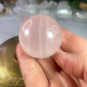 May include: A polished pink rose quartz sphere with white banding. The sphere is smooth and translucent.