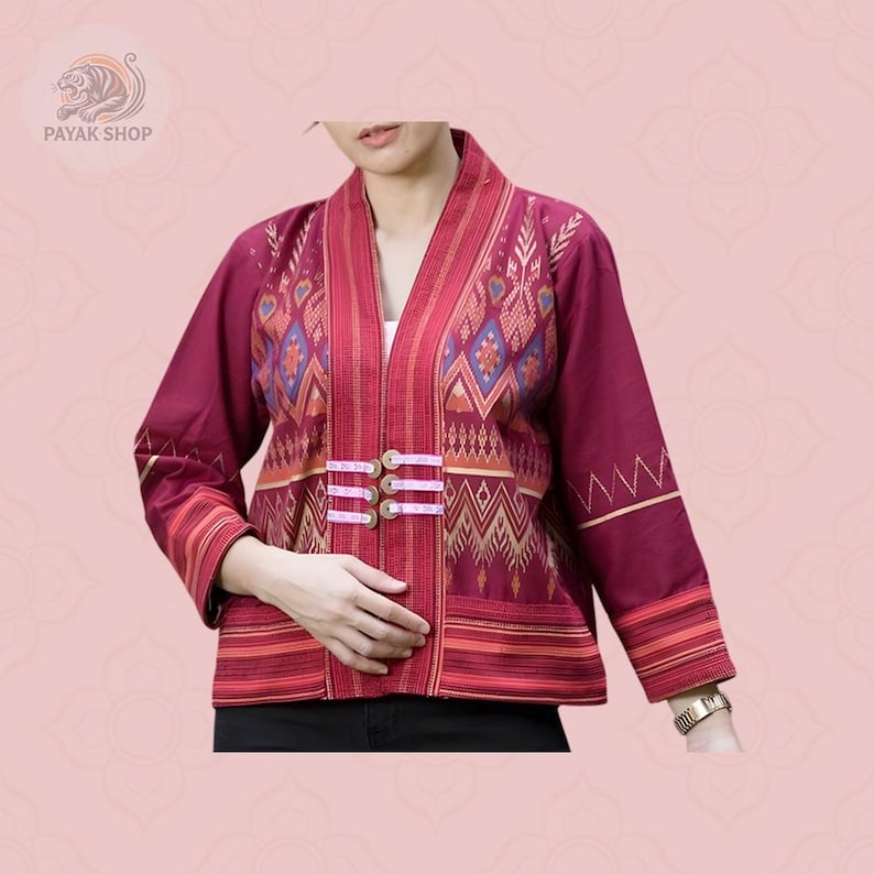 May include: A burgundy jacket with an open front and intricate geometric patterns in shades of red, gold, and blue. The jacket features three pink closures and long sleeves. The jacket is part of the Payak Shop collection.