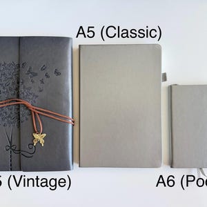 May include: Three notebooks of varying sizes are displayed. The largest, labeled "A5 (Vintage)", is dark gray with an embossed tree and butterfly design, secured with a brown cord and a butterfly charm. The "A5 (Classic)" and "A6 (Pocket)" notebooks are light gray.