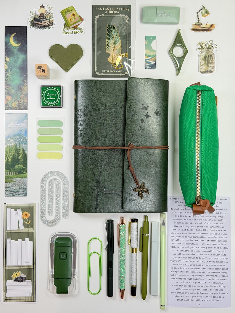 May include: An assortment of stationery and decorative items in shades of green and white. Includes a green journal, pens, stickers, a pencil case, and a metal bookmark with a feather design. The items are arranged on a white surface.