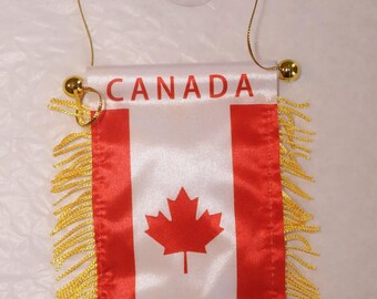 May include: A small Canadian flag with the word "CANADA" printed at the top. The flag features the Canadian maple leaf emblem in red on a white background, with red vertical stripes on each side. It has gold fringe and a gold hanging cord.