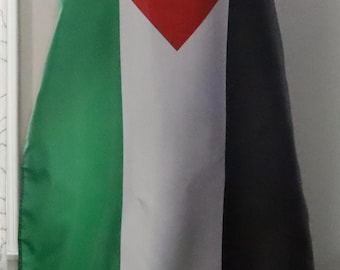 May include: A cape featuring the Palestinian flag design. The cape has a red triangle at the top, followed by a white stripe, a green stripe, and a black stripe. The cape is worn by a person.