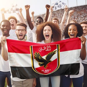 Peut inclure: Un groupe de supporters enthousiastes brandit un drapeau rouge, blanc et noir avec un logo d'équipe. Le drapeau présente un écusson avec un aigle noir et du texte arabe. Les fans, vêtus de chemises blanches, encouragent lors d'un événement sportif.