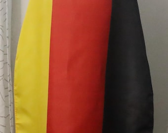 May include: A cape with vertical stripes of yellow, red, and black. The cape is draped over a person, with the back of their head and shoulders visible. The colors are vibrant and the fabric appears to be smooth.