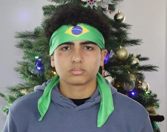 May include: A green headband with the Brazilian flag design, worn by a person. The headband is paired with a blue hoodie. A Christmas tree with ornaments is in the background.