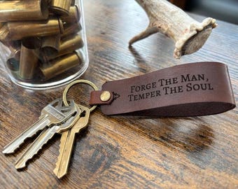 May include: Brown leather keychain with a metal ring and three keys. The keychain has the text "Forge The Man, Temper The Soul" engraved on it.