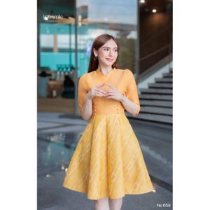 Puede incluir: Un vestido amarillo con cuello mandarín y mangas tres cuartos. El corpiño tiene tres botones y la falda presenta un estampado de diamantes. El vestido llega a la rodilla y tiene una silueta acampanada. El texto "No.659" es visible.