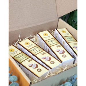May include: A gift box filled with several boxes of PINDARA Coconut Oil Serum. The boxes are white and gold with images of coconuts and the text "COCONUT OIL SERUM". The box is filled with straw.