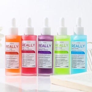 May include: Five bottles of body dose AHA solution in orange, red, purple, green, and blue. Each bottle has a white dropper top and a label with the word "REALLY" in large white letters. The bottles are arranged in a row.