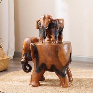 Könnte beinhalten: Ein handgefertigter Elefantenhocker aus Holz mit einer passenden Elefantenskulptur. Der Hocker ist braun mit schwarzen Akzenten, die Elefantenskulptur ist aufwendig geschnitzt. Der Hocker steht auf einem gewebten Jute-Teppich.