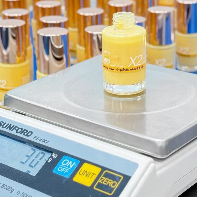 May include: A clear glass bottle filled with yellow liquid, labeled "COLLAGEN PLUS X2", sits on a digital scale. The scale reads 30 kg. Other bottles with gold and silver lids are in the background.