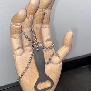 May include: A silver bottle opener on a chain, held by a wooden hand.