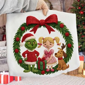 Puede incluir: Cojín blanco con temática navideña con un diseño bordado. El diseño presenta al Grinch, una niña y un perro dentro de una corona verde con bayas rojas y un gran lazo rojo. El Grinch lleva un gorro de Papá Noel y un atuendo rojo.