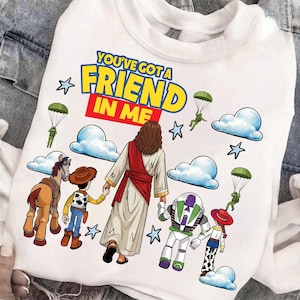 Puede incluir: Sudadera blanca con la frase "YOU'VE GOT A FRIEND IN ME" en amarillo y azul. El diseño incluye personajes de dibujos animados, nubes, estrellas y figuras con paracaídas. La sudadera tiene cuello redondo.