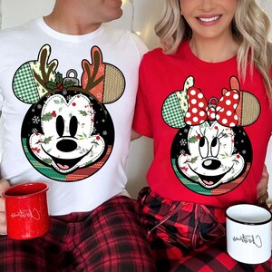 Könnte beinhalten: Zwei passende Weihnachtsshirts. Eines ist weiß mit einem Mickey Mouse-Ornament-Design mit Geweih, das andere ist rot mit einem Minnie Mouse-Ornament-Design mit einer Schleife. Beide Designs haben einen schwarzen Hintergrund mit Stechpalmen und Schneeflocken.