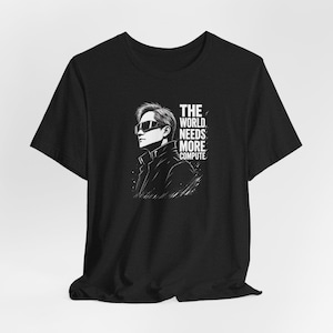 以下が含まれることがあります： サングラスとジャケットを着た人物の白黒イラストが描かれた黒いTシャツ。「THE WORLD NEEDS MORE COMPUTE」の文字が右側にプリントされています。