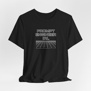 May include: Black t-shirt with the text "PROMPT ENGINEER IRL" in white, above a white grid design. The shirt has short sleeves and a crew neck, and is made of a soft material.