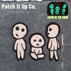 May include: Embroidered patches with three white figures with black outlines and facial features. The patches include the text "Patch It Up Co." and "Embroidery". A smaller patch shows the figures glowing green with the text "Glow in the Dark".