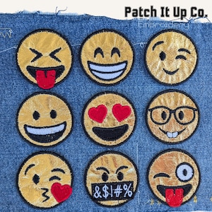 May include: Nine embroidered emoji patches with various expressions, including laughing, winking, and hearts for eyes. The patches are gold with black and red details, displayed on a denim background. The text "Patch It Up Co." is at the top.