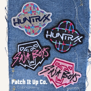 Könnte beinhalten: Vier gestickte Aufnäher auf Denim. Zwei Aufnäher lesen "HUNTRX" mit einem Karomuster, einer in Grau und der andere in Schwarz. Die anderen beiden Aufnäher lesen "Stit Boys" mit einer Tigergrafik, einer in Schwarz und Weiß, die andere in Rosa.